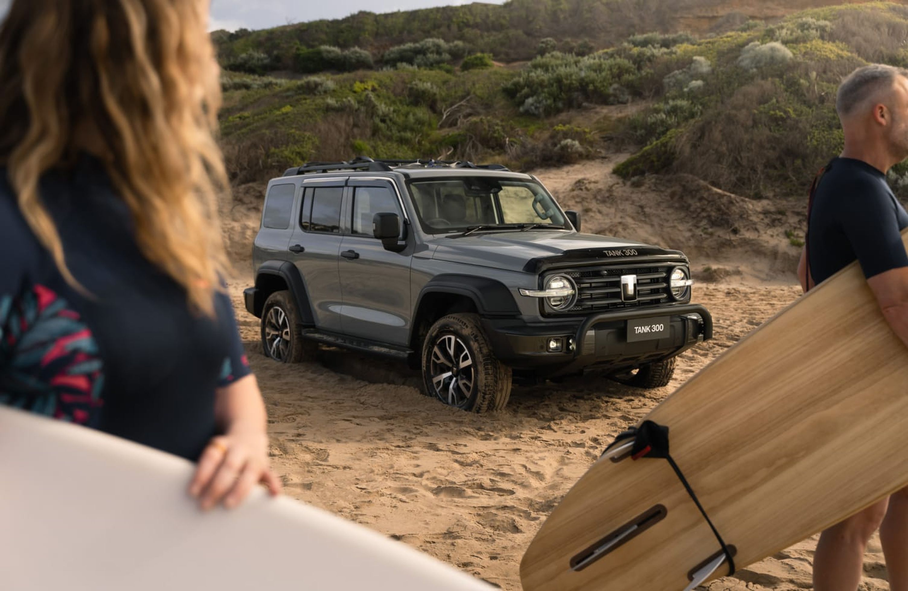 Fossil Grey GWM Tank 300 with a black nudge bar parked on the sand with people walking by carrying surfboards