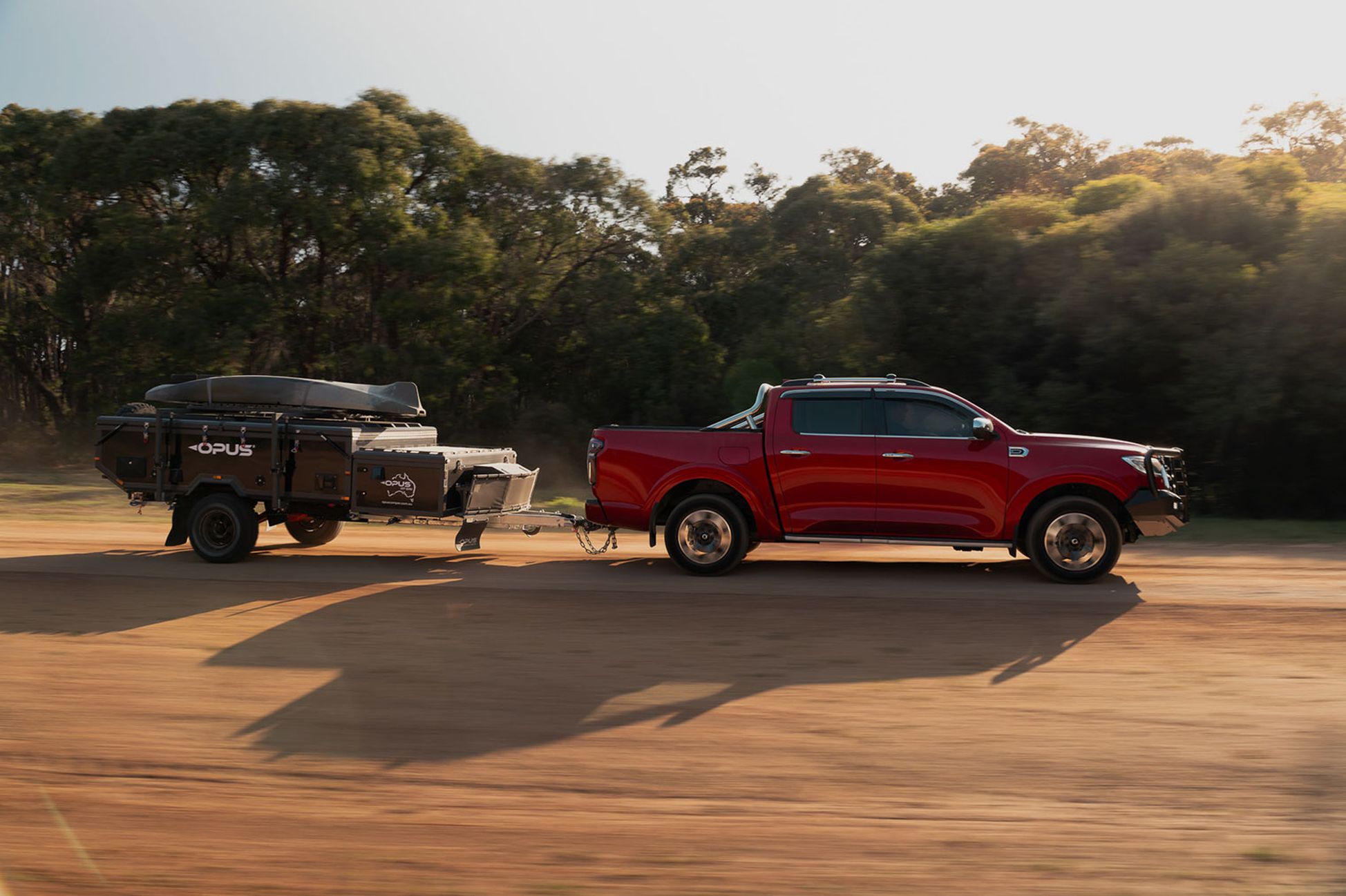 Scarlet Red GWM Cannon ute with a blakc bull bar towing a caravan along a dirt road