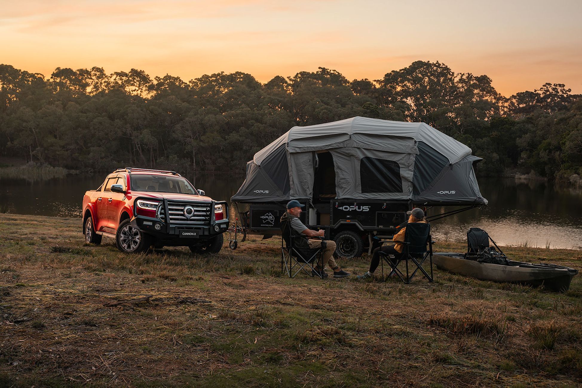Scarlet Red GWM Cannon ute parked with the caravan unhitched and the owners sitting on foldout chairs next to their canoe