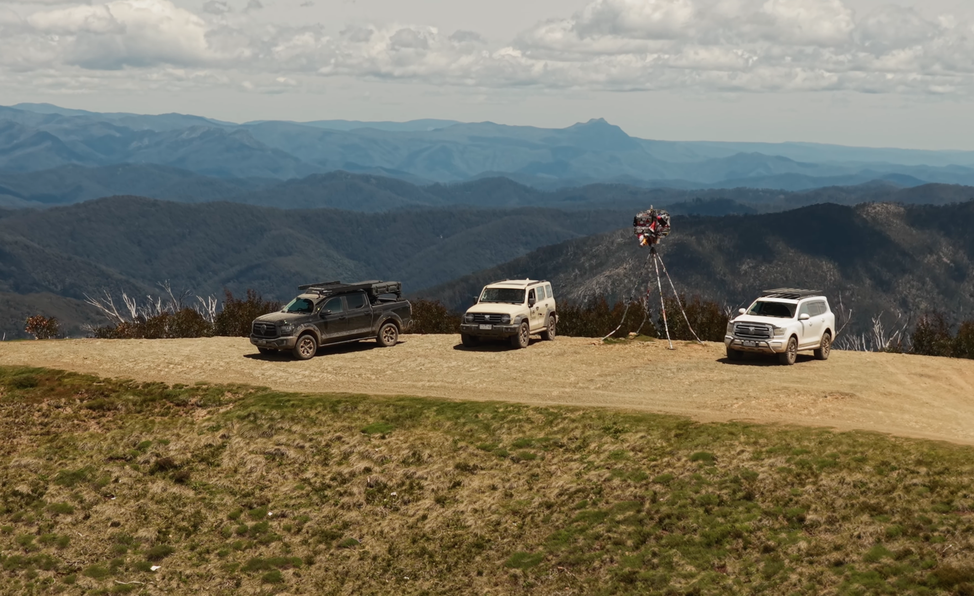 Three SUVs parked on a mountain lookout with a scenic view of rolling hills and a cloudy sky in the background.