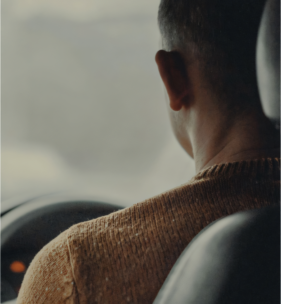 Looking over the shoulder of a man in a brown knitted jumper in his car
