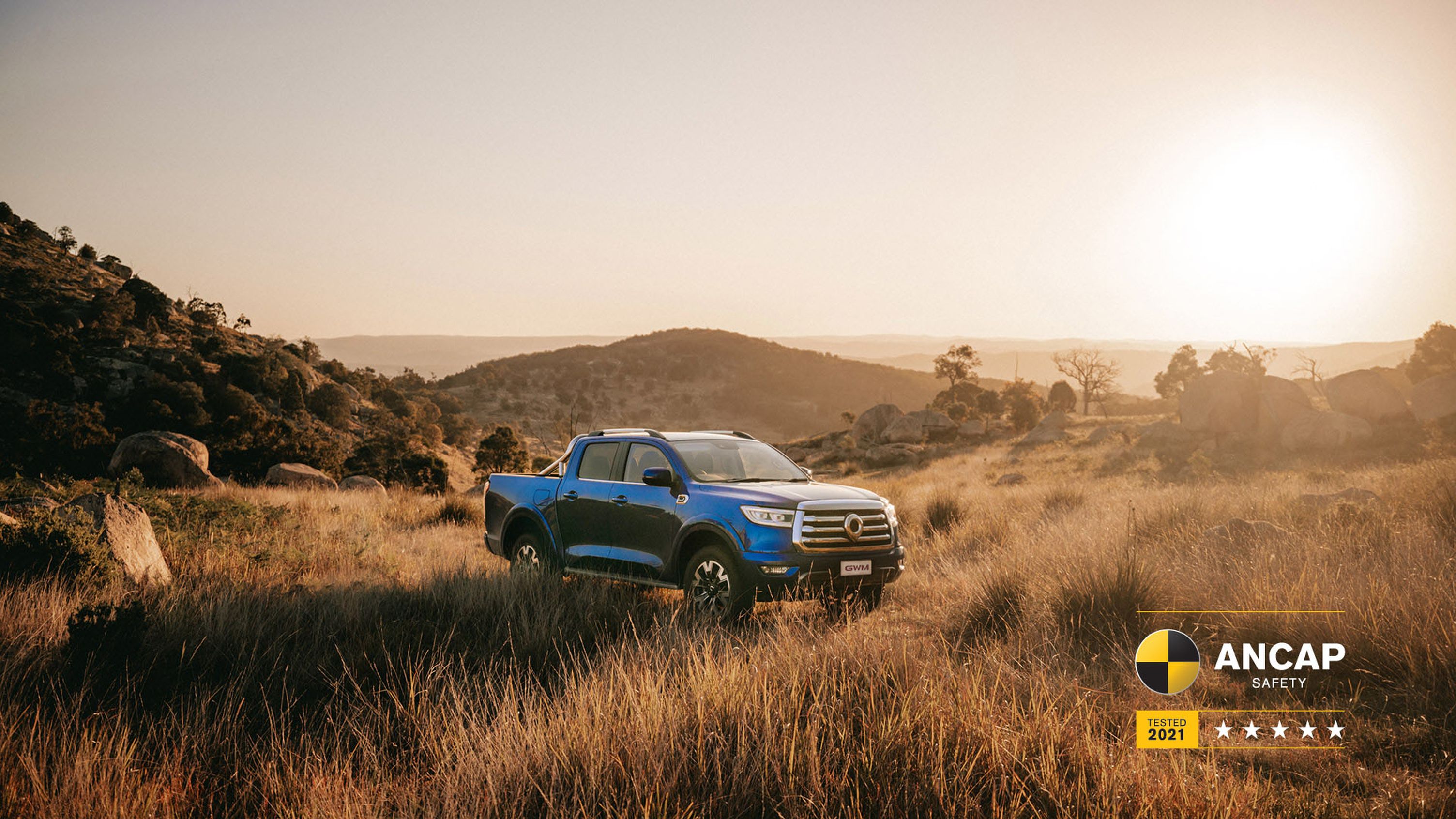 Sapphire Blue GWM Ute Cannon parked in the grassy fields with hills in the background and the sun setting