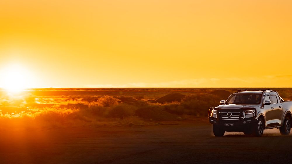 Slate Grey GWM Ute Cannon with a black bull bar driving through the desert as the sunsets in the background
