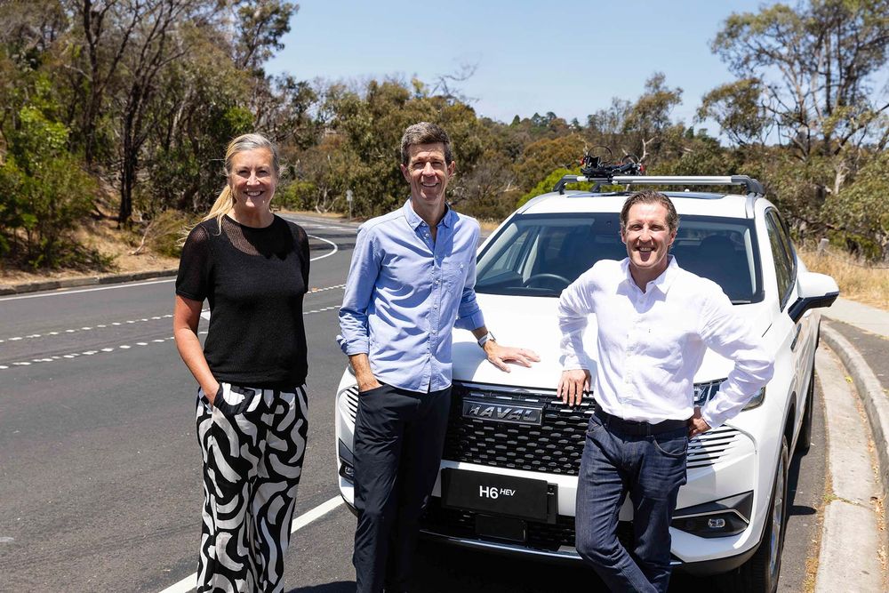 Auscycling and GWM members leaning on a Pearl White GWM Haval H6 Hybrid on a road full of dry bushes