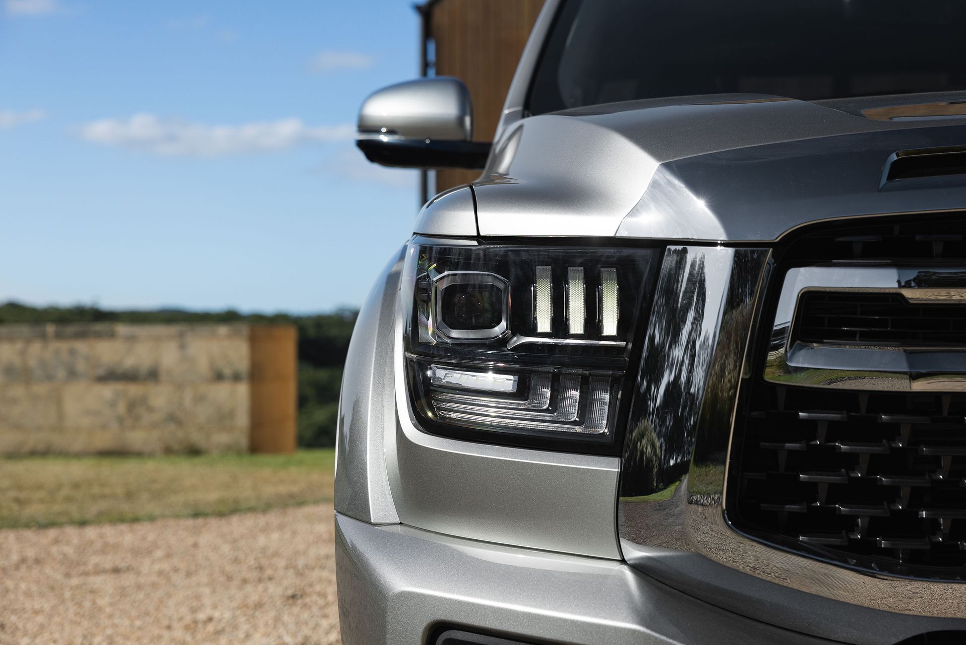 A GWM Cannon Alpha in Onyx Silver, GWM's larger ute available in hybrid, parked with a farm backdrop with the focus on the headlight