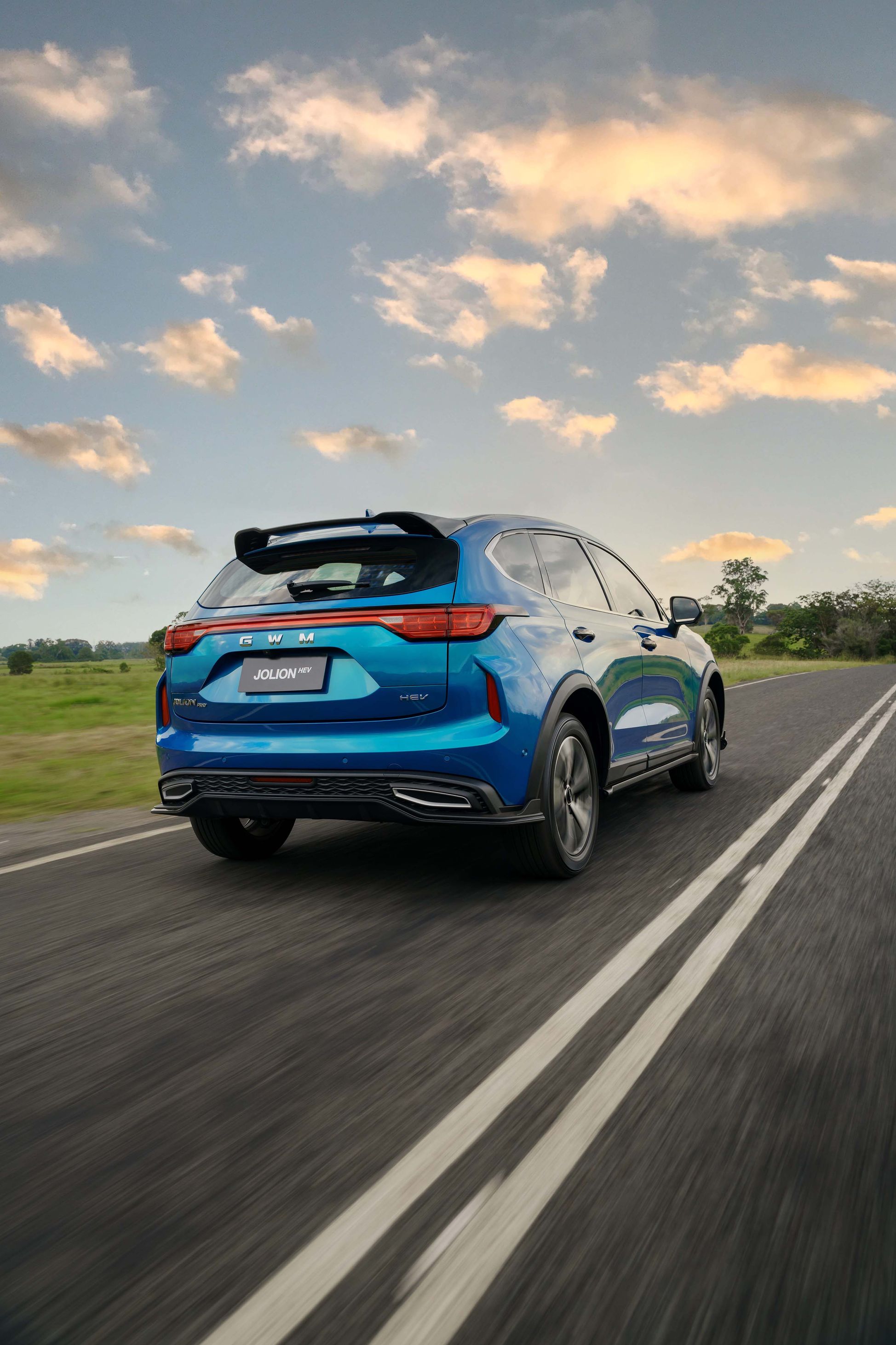 The rear of an Aurora Green GWM Haval Jolion Hybrid driving with green grass on the side of the road