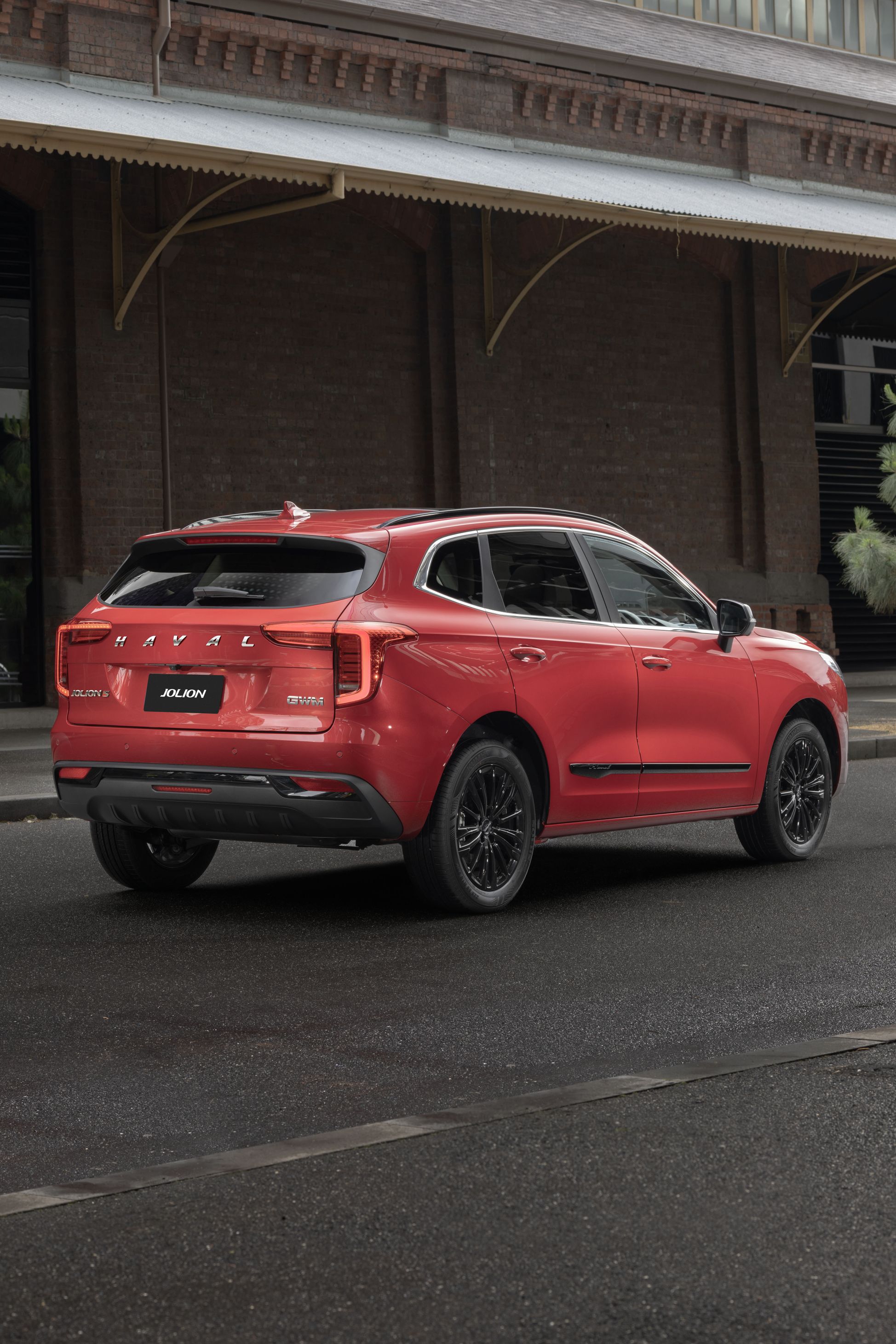 Mars Red GWm Haval Jolion parked in the city next to a Victorian era style brick building