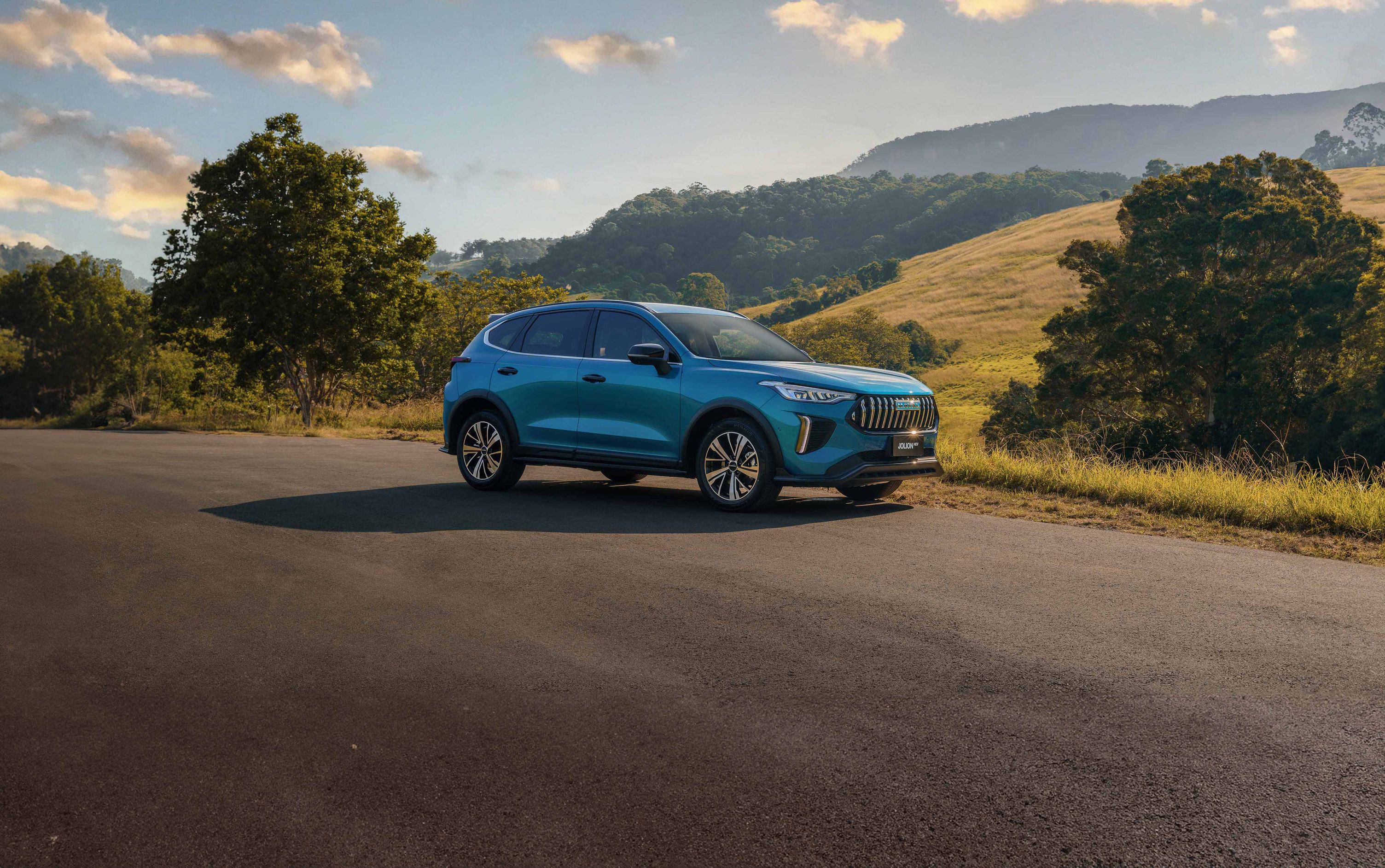 An Aurora Green GWM Haval Jolion Hybrid parked in front of a hill with the sunsetting