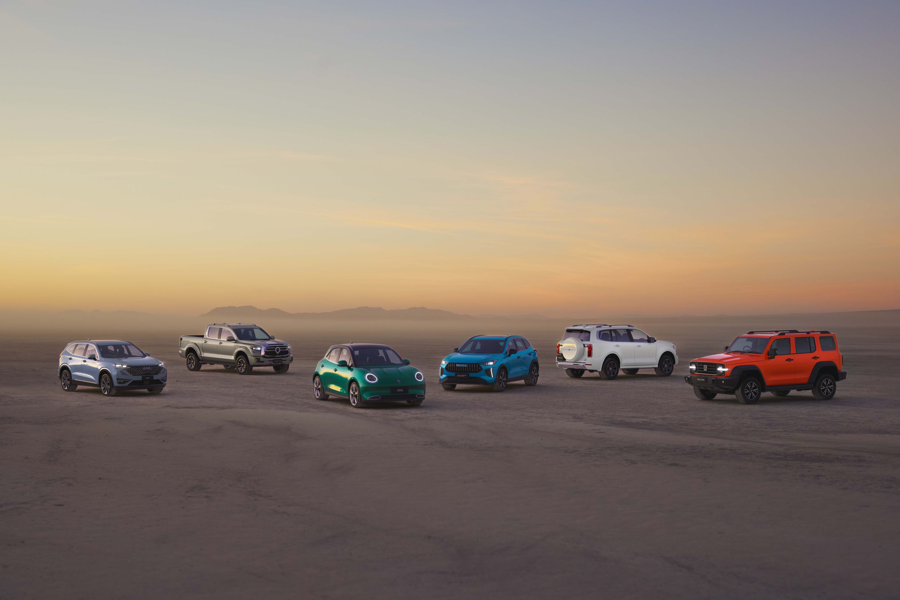 The whole GWM vehcle range including GWM Haval SUV, GWM Ute Cannon utes, GWM Ora EVs, and GWM Tank off-road SUVs lined up in the dessert like environment as the sun is setting
