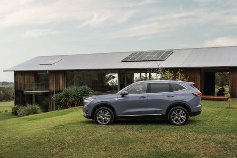 A GWM Haval H6 Hybrid in Ayers Grey parked in front of a modern wood style house with solar panels