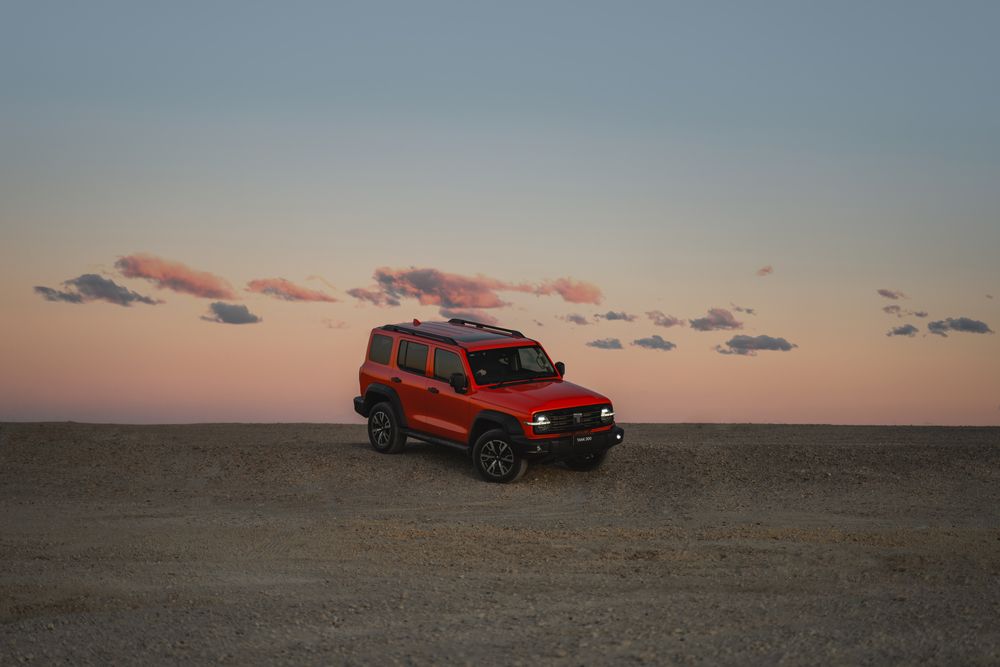 Dusk orange Tank 300 parked on top of a gravel hill with the sunset sky in the background