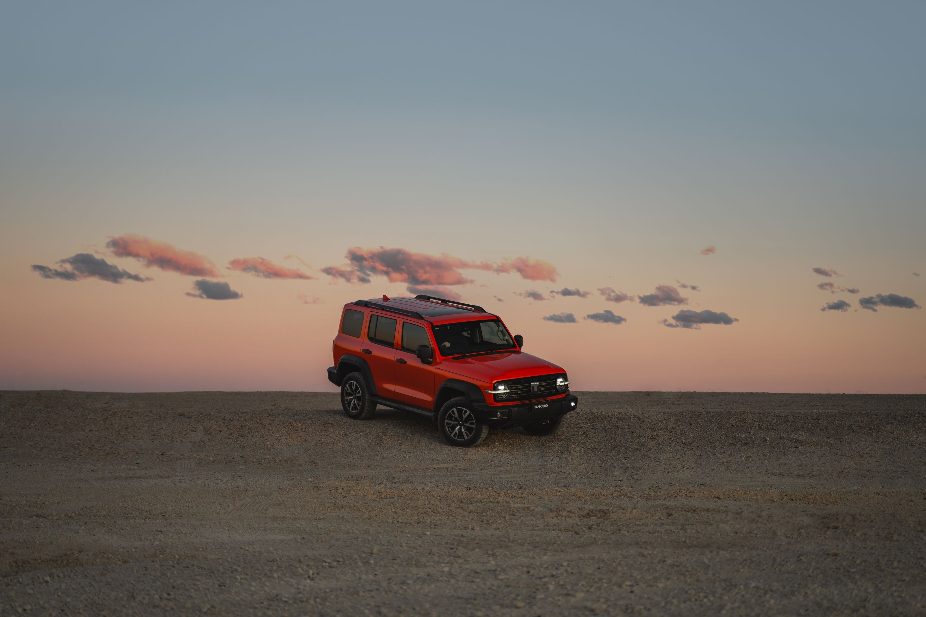 Dusk orange Tank 300 parked on top of a gravel hill with the sunset sky in the background
