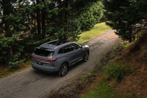 A GWM Haval H6 Hybrid in Ayers Grey driving on gravel road emerging from the trees