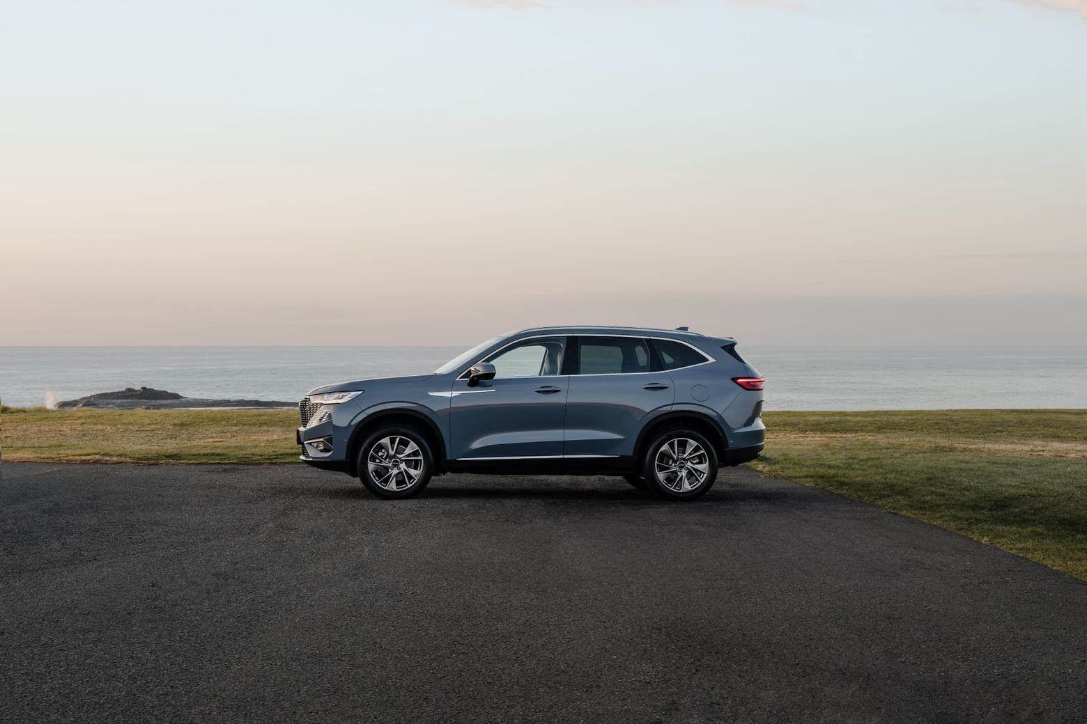 GWM Haval H6 Hybrid in Ayers Grey parked parallel to the ocean in the background