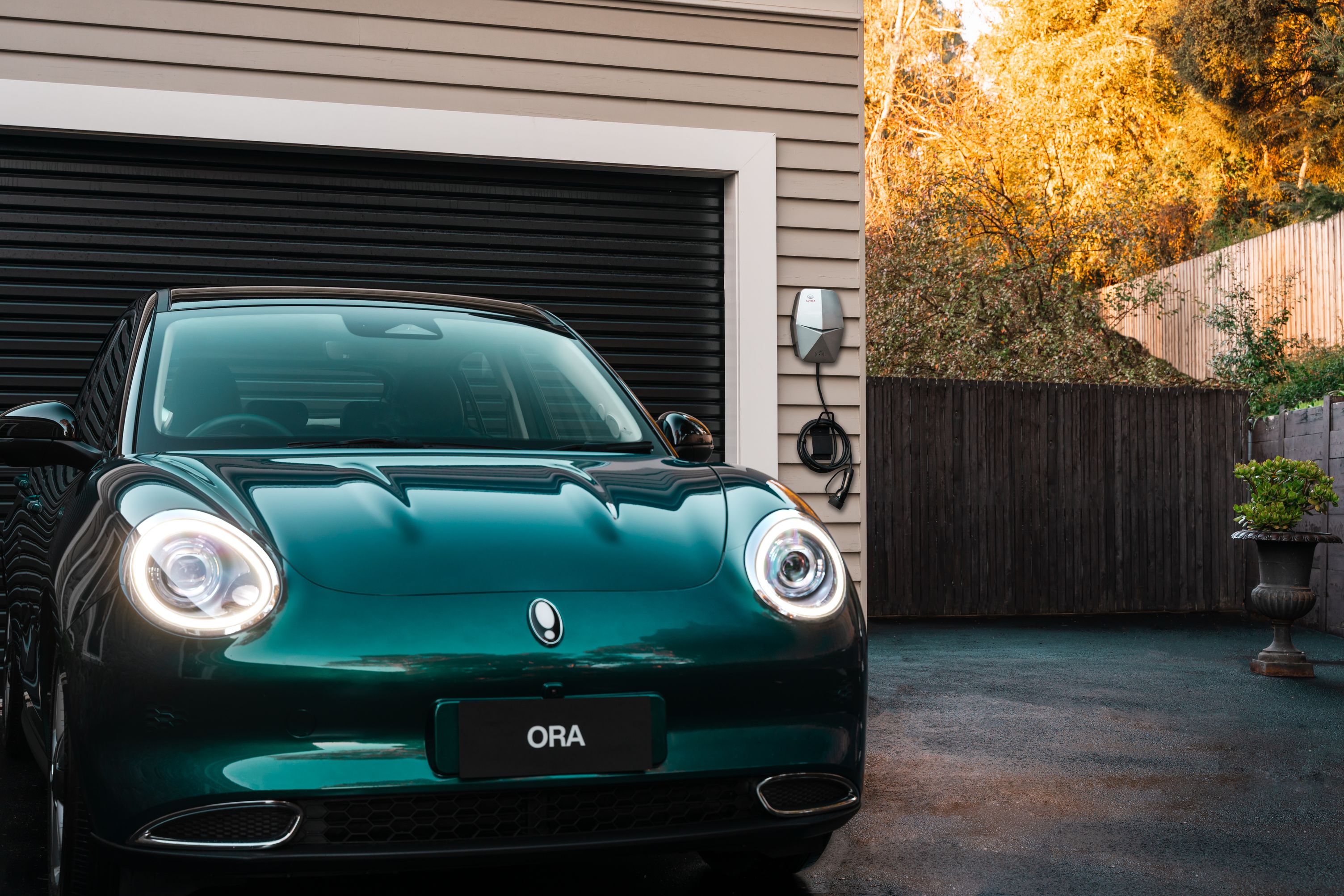Aurora Green Ora parked outside of a house with the GWM charger mounted on the garage wall